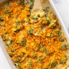 wooden spoon stuck into broccoli casserole with crushed crackers on top.
