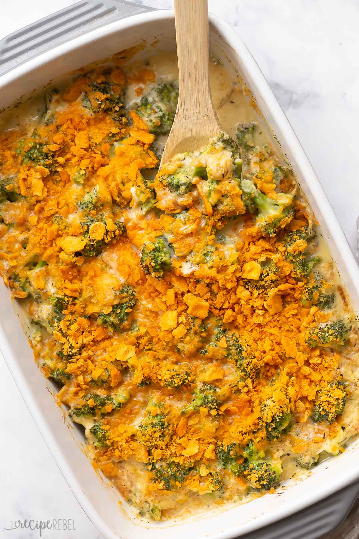 wooden spoon stuck into broccoli casserole with crushed crackers on top.