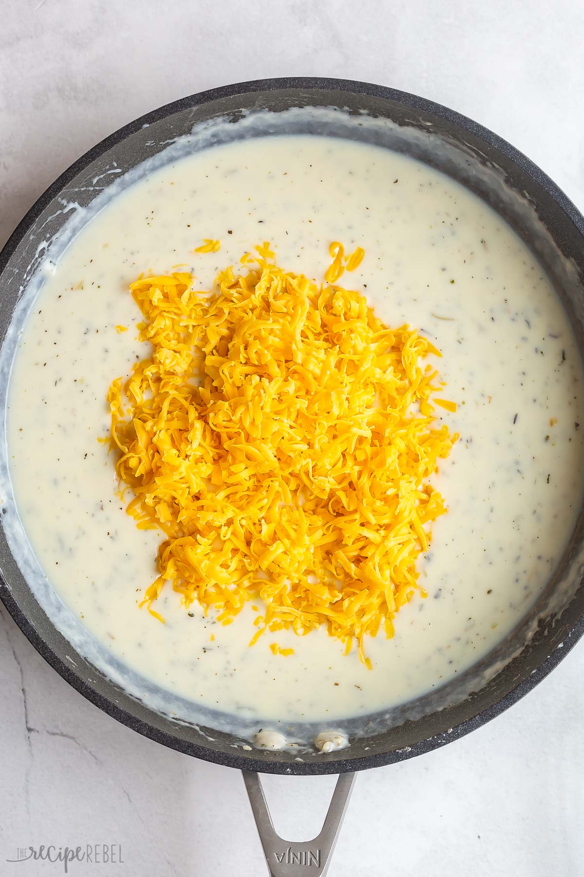creamy sauce in skillet with shredded cheese added.