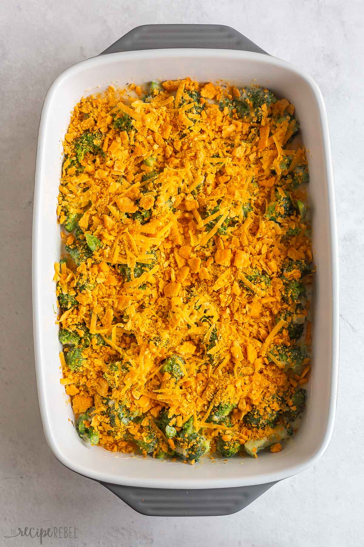 broccoli in casserole dish with sauce shredded cheddar cheese and crushed crackers.