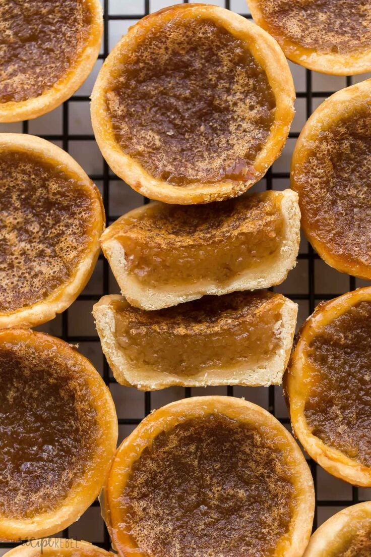 These Butter Tarts are a Canadian classic that comes together with just 25 minutes of prep! Homemade pastry shells are filled with a rich, brown sugar (raisins optional!), then baked until buttery and flaky on the inside and gooey on the inside. #baking #recipes | canadian recipes | tart shells | pie crust | homemade pastry | christmas treats | christmas baking | dessert recipes close up image of butter tart cut in half on cooling rack