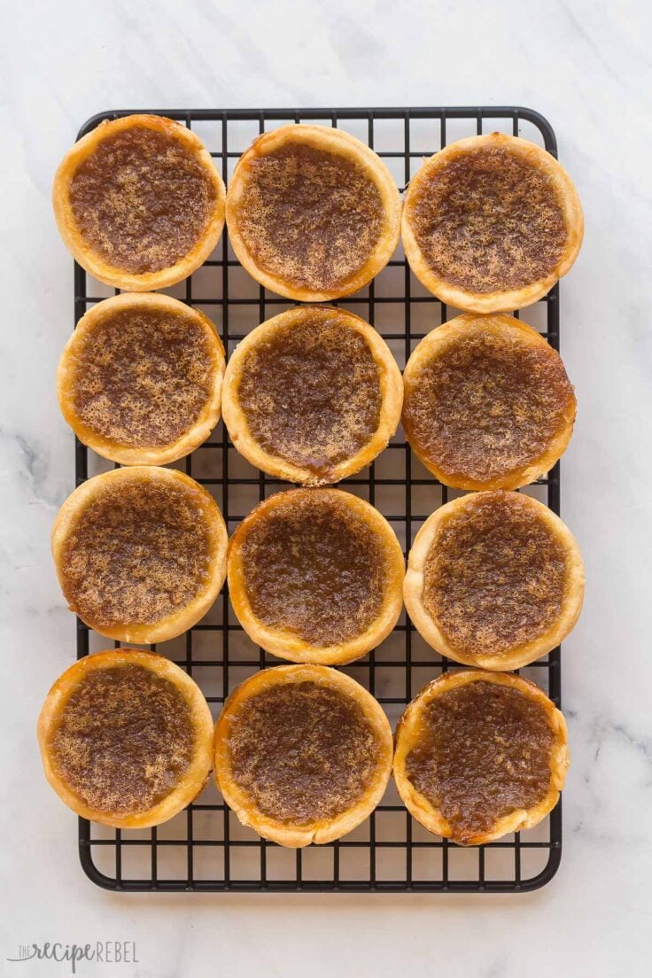 These Butter Tarts are a Canadian classic that comes together with just 25 minutes of prep! Homemade pastry shells are filled with a rich, brown sugar (raisins optional!), then baked until buttery and flaky on the inside and gooey on the inside. #baking #recipes | canadian recipes | tart shells | pie crust | homemade pastry | christmas treats | christmas baking | dessert recipes finished butter tarts on black cooling rack