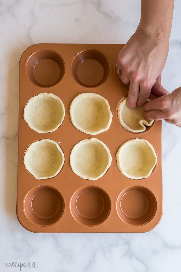 pie pastry being pressed into muffin pan to make tart shells