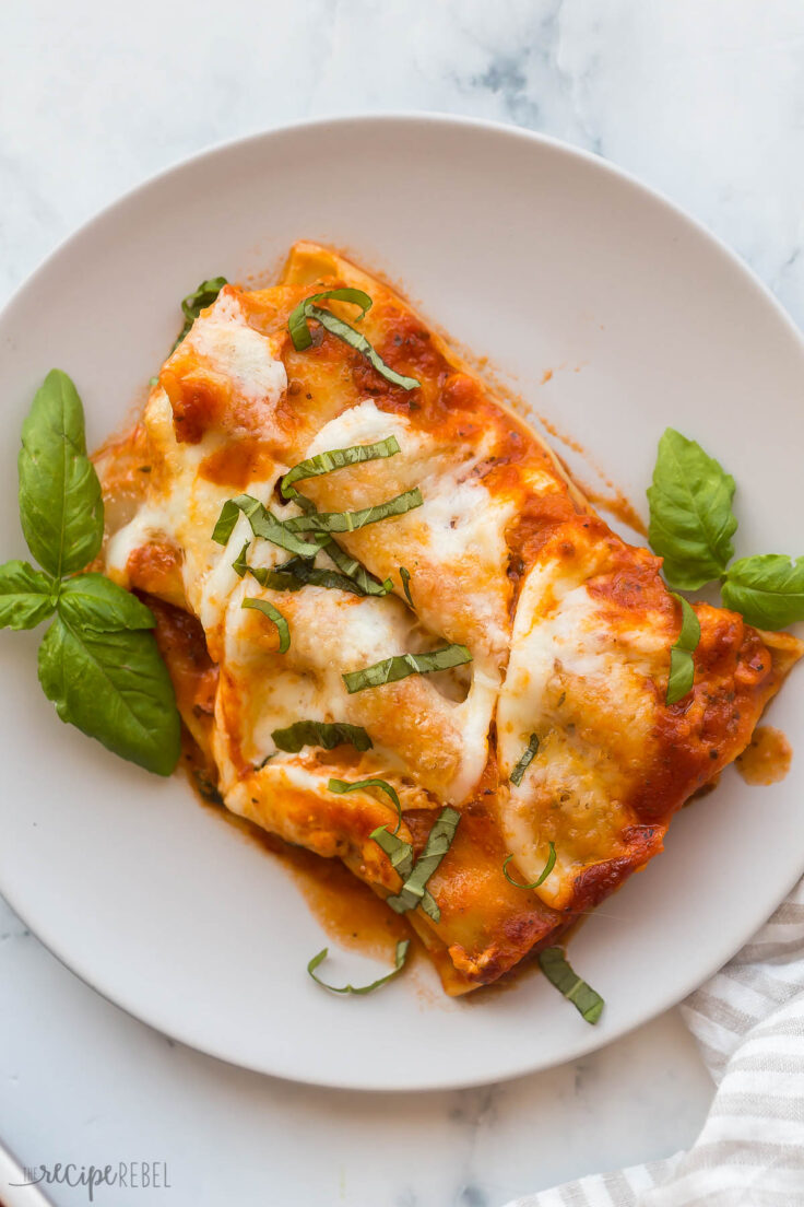two cheese cannelloni on a grey plate with fresh basil