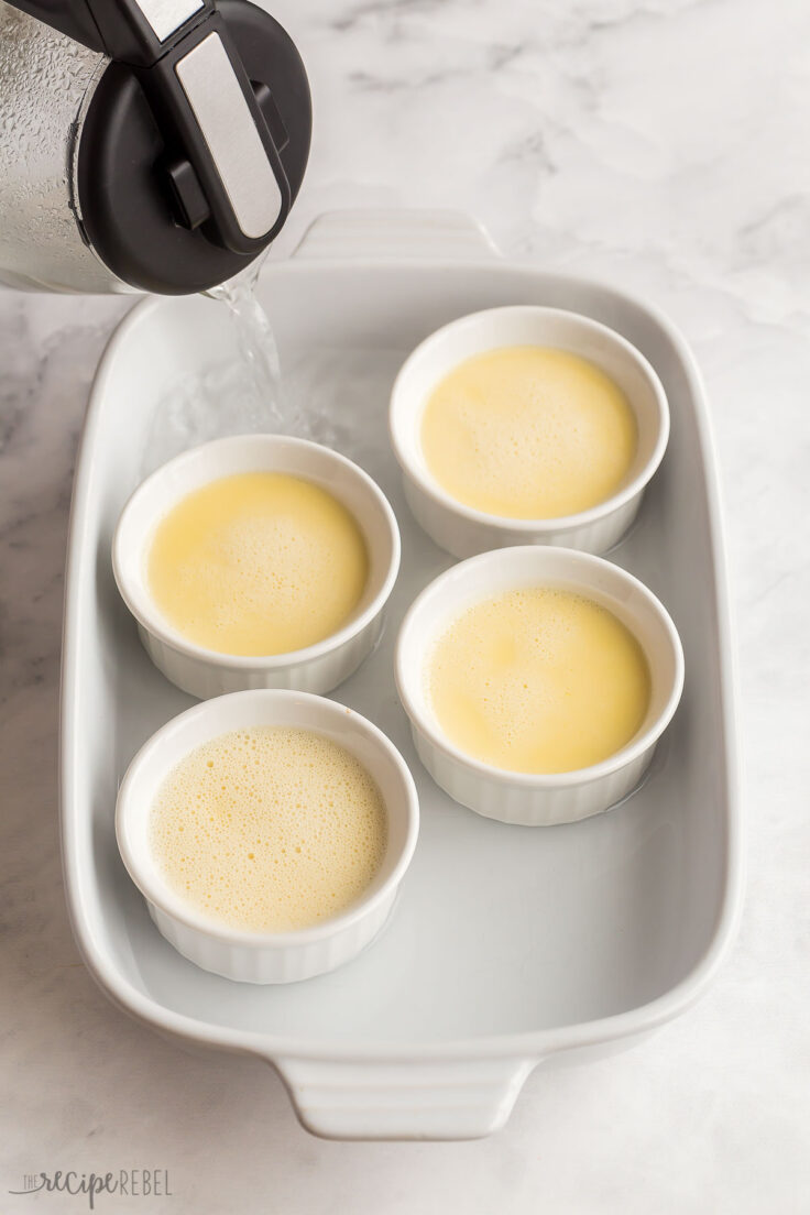 ramekins in a baking dish with hot water from a kettle being added around ramekins