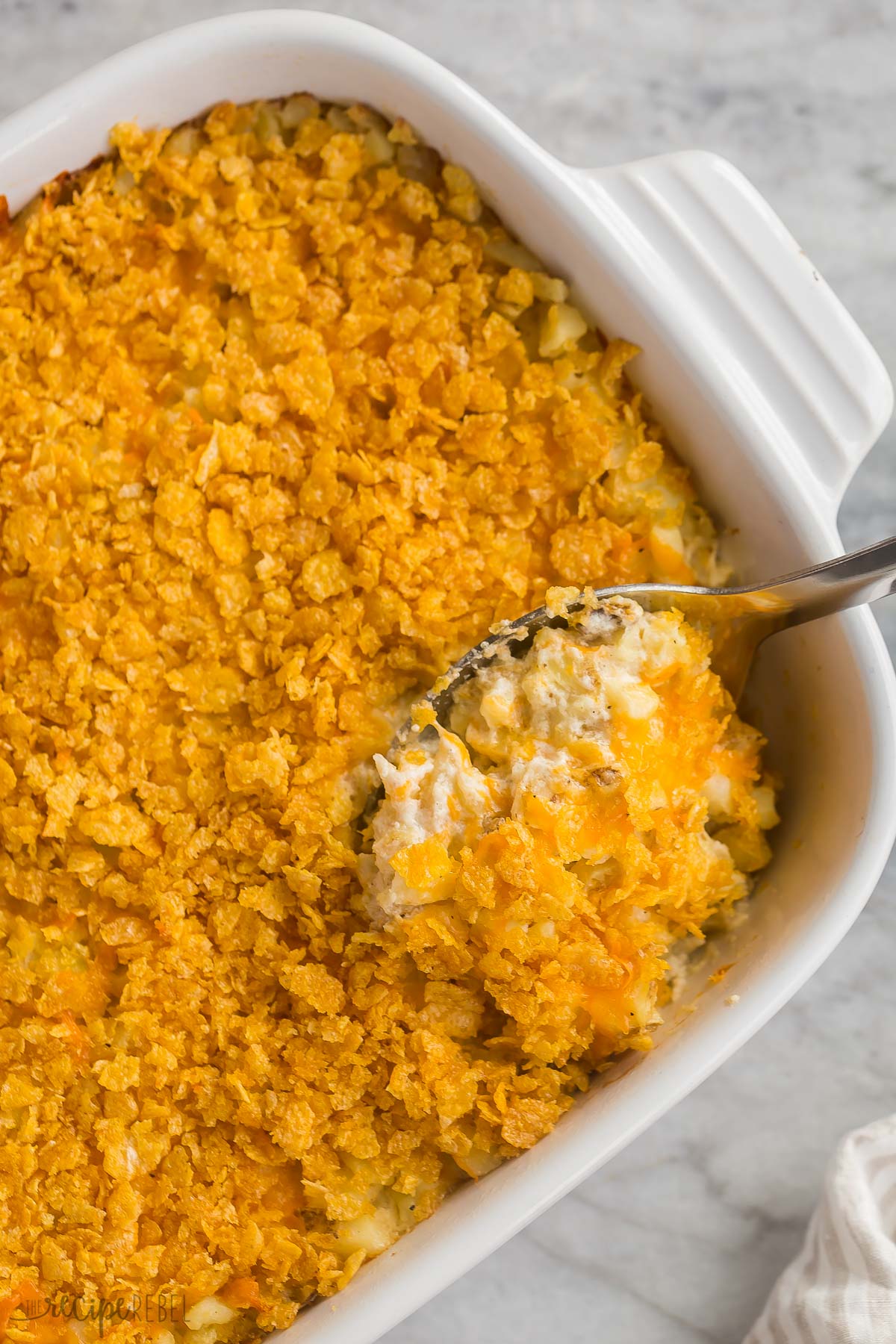 close up image of metal spoon scooping hashbrown casserole from baking dish