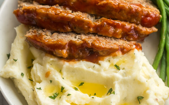 square image of three slices of instant pot meatloaf on mashed potatoes