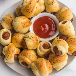 pigs in a blanket on a plate with bowl of ketchup in the middle