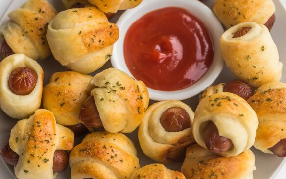 pigs in a blanket on a plate with bowl of ketchup in the middle