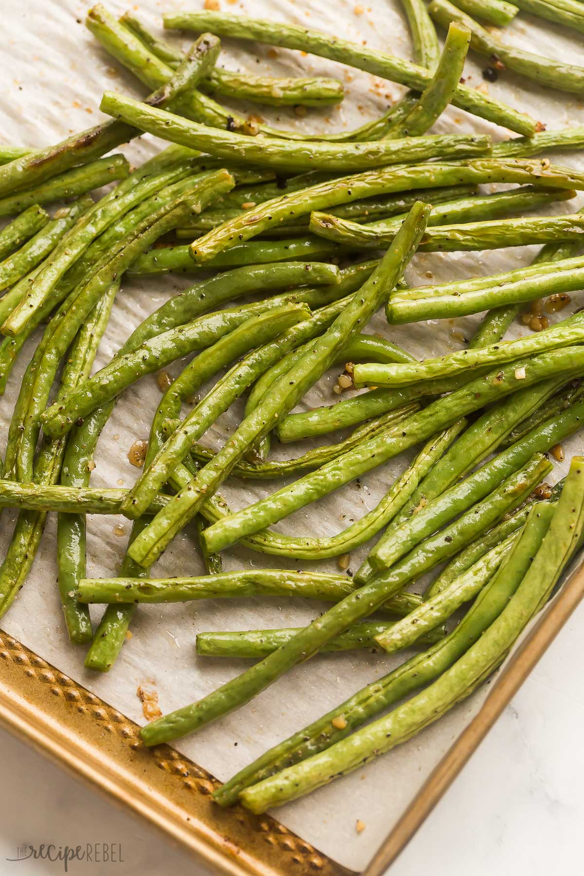 These Roasted Green Beans are a simple and versatile side dish that takes just 5 minutes to prep! This 5-ingredient recipe is made with fresh green beans that are roasted to crisp-tender perfection! #recipes #dinner #sides | side dish recipes | vegetable side dishes | how to cook green beans | thanksgiving dinner | christmas dinner | easy recipes | easy meals close up image of roasted green beans on baking sheet