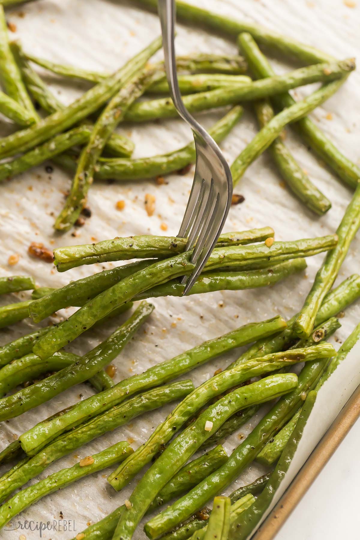 fork picking up roasted green beans off of a baking sheet