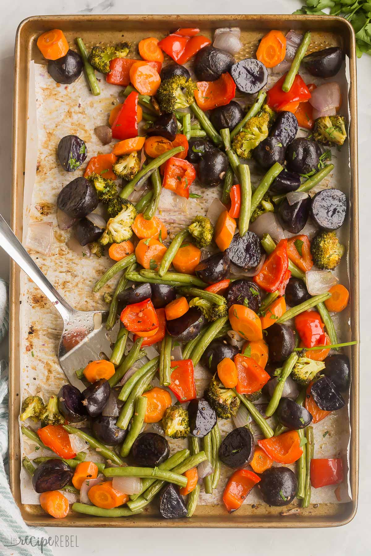 These Roasted Vegetables are made up of a colorful blend of veggies that are perfectly seasoned with fresh garlic, butter, cracked pepper, and parsley! This 5-minute side dish pairs perfectly with any meal! #vegetables #recipe | side dish recipes | healthy recipes | healthy dinner | vegetarian | easy dinner ideas metal spatula scooping roasted vegetables from pan