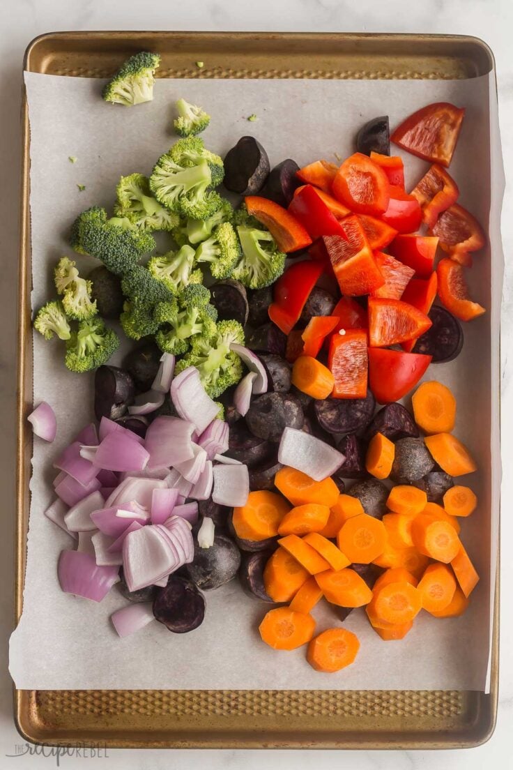 uncooked broccoli potatoes pepper carrots and onion on a sheet pan