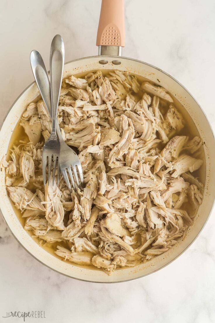 overhead image of shredded chicken in white skillet with two forks