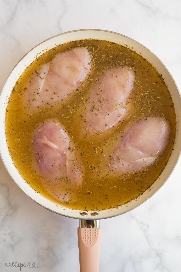 uncooked chicken breasts in a skillet with broth and seasonings