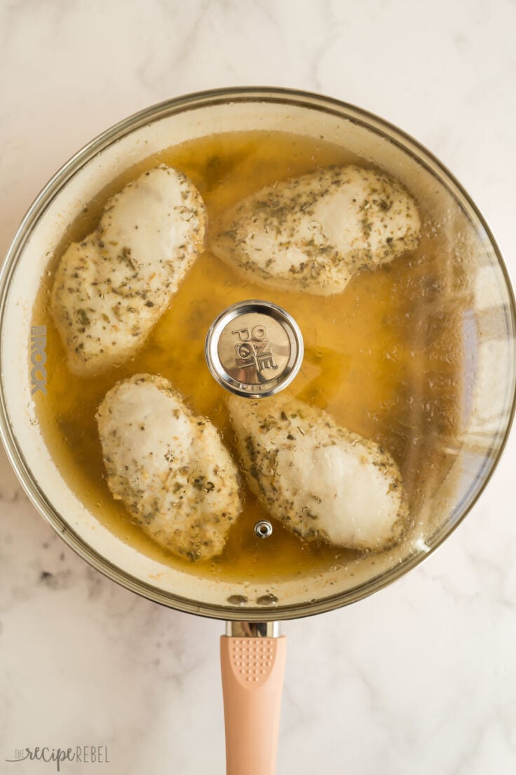 cooked chicken breasts in broth with glass lid on pan