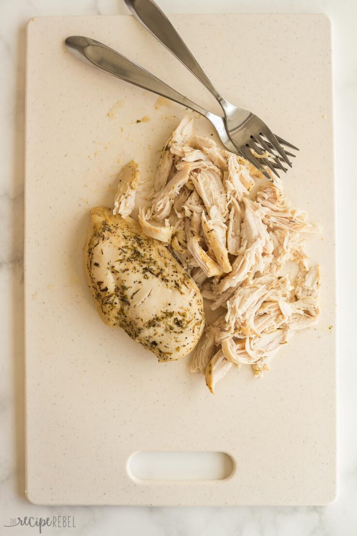 two forks shredding chicken on a white cutting board