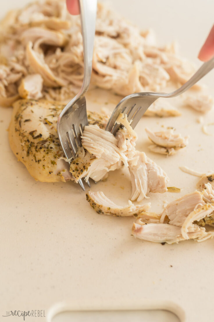 two forks pulling chicken on a cutting board