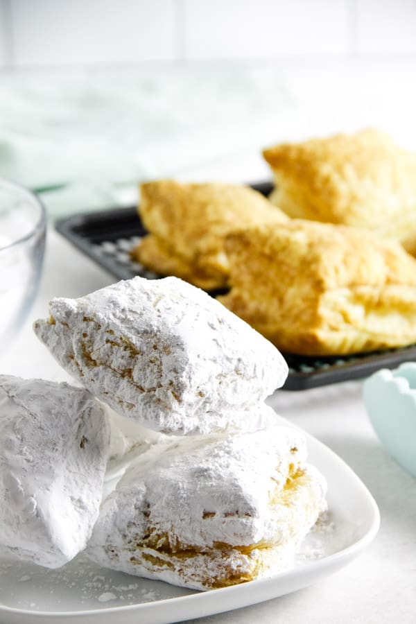 air fryer beignets coated in powdered sugar stacked on plate