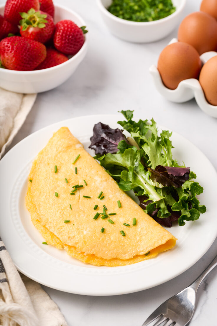 cheese omelette on a white plate with greens on the side