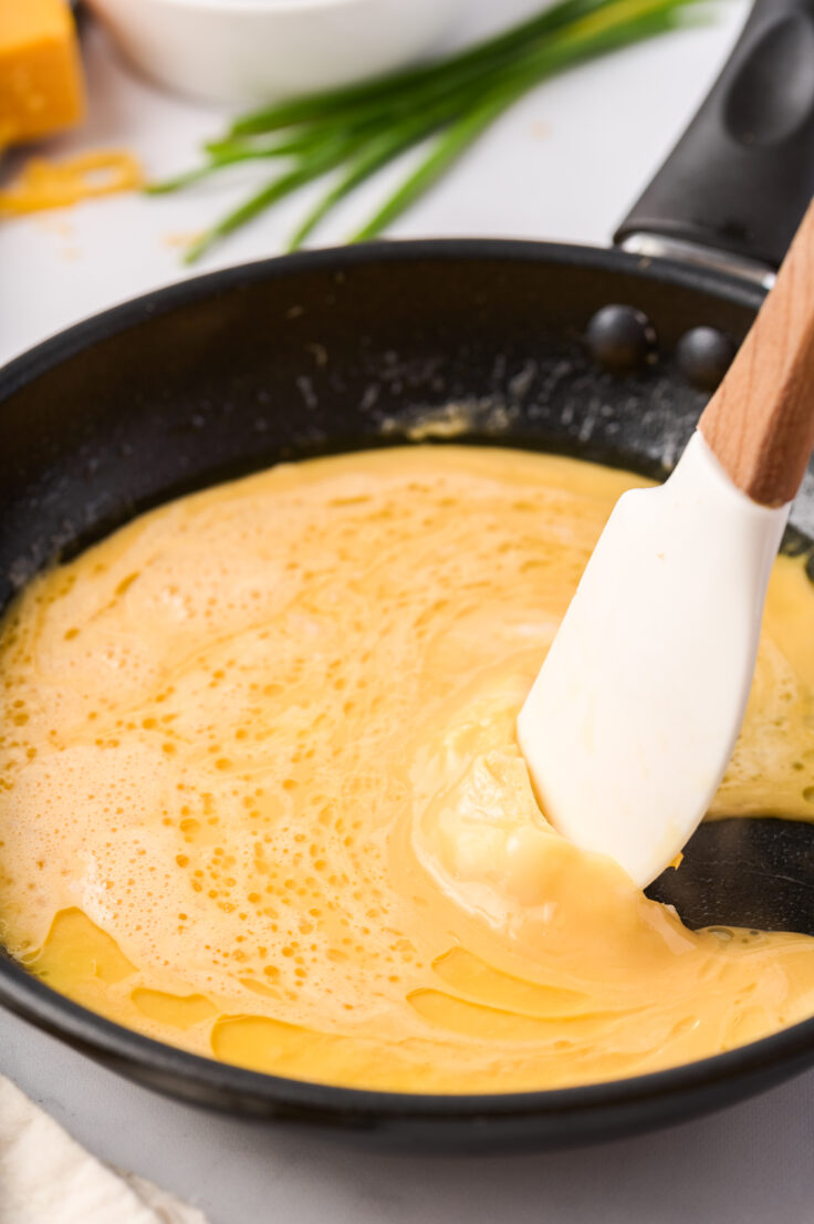 spatula moving cooked portion of egg to allow runny egg to run under