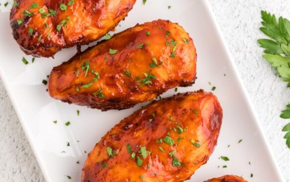 A row of barbecue chicken breasts on a plate.
