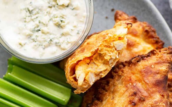 Buffalo chicken empanadas on a plate next to celery sticks and blue cheese dressing.