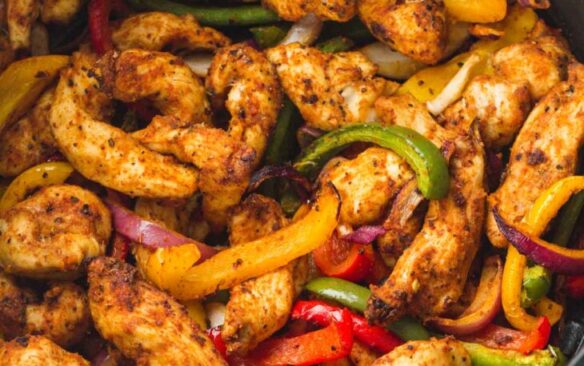 Chicken fajitas with colored peppers in the basket of an air fryer.