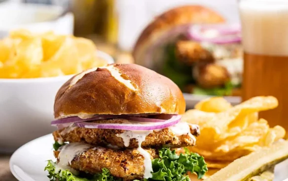 A chicken schnitzel sandwich on a plate next to French fries.