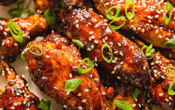 Sticky air fryer chicken wings sprinkled with sesame seeds on a plate.