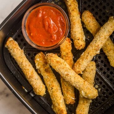 mozzarella sticks in air fryer with bowl of pizza sauce