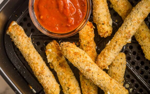 mozzarella sticks in air fryer with bowl of pizza sauce