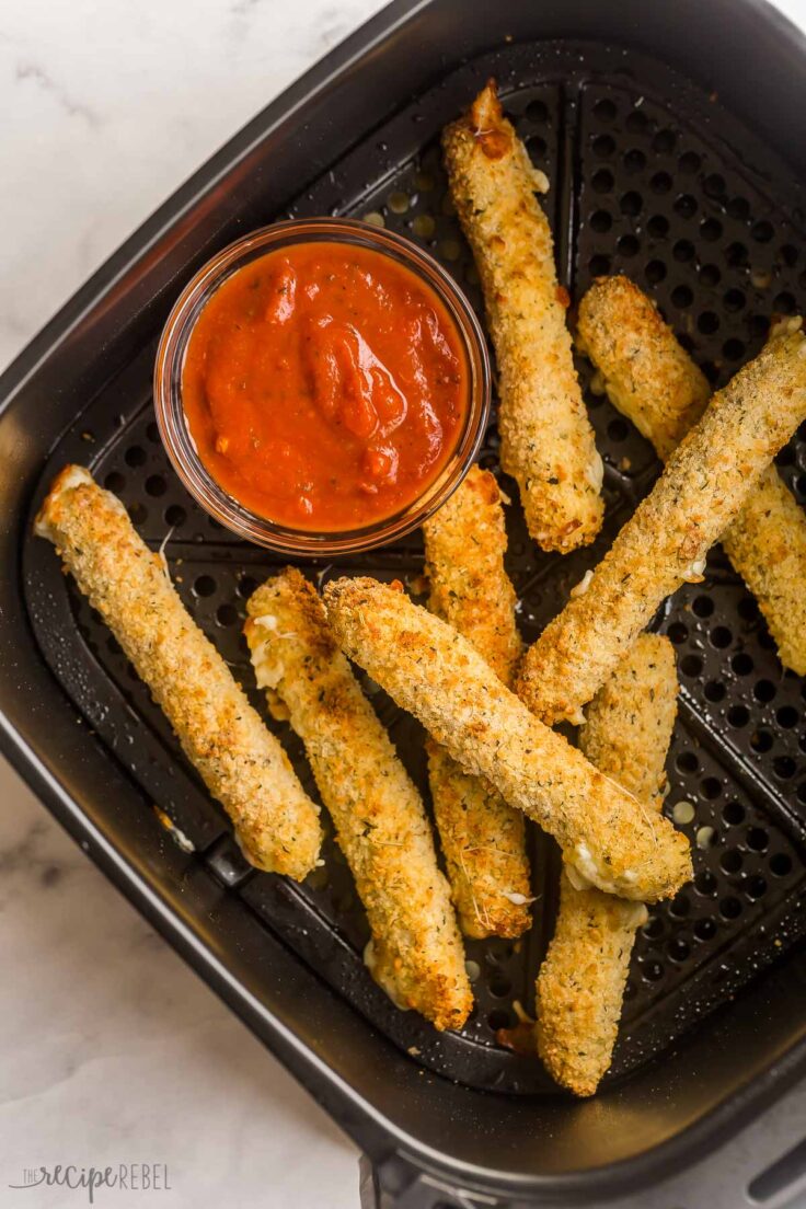 mozzarella sticks in air fryer with bowl of pizza sauce