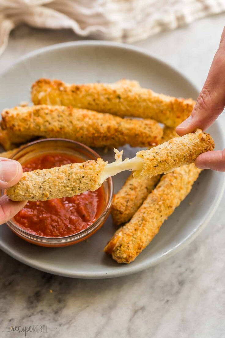 fingers pulling apart mozzarella stick to reveal cheese