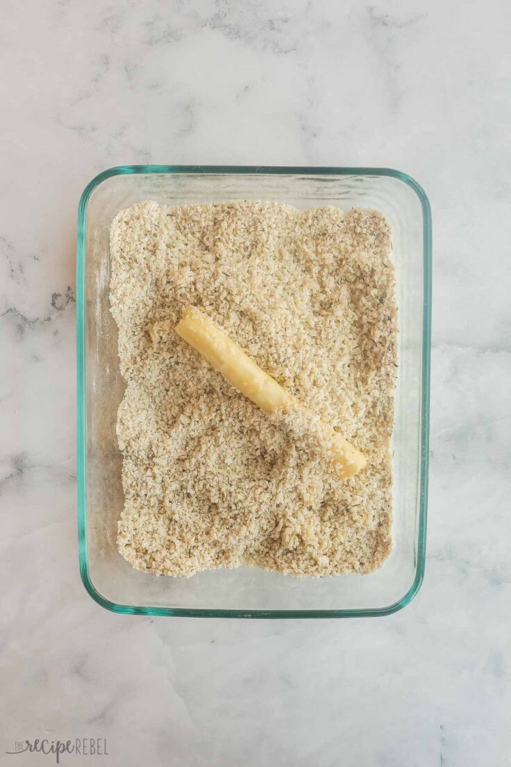 egg coated mozzarella stick being coated in bread crumbs