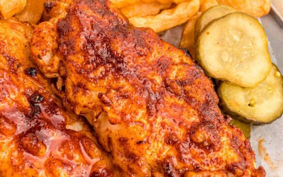 Nashville hot chicken served next to crinkle fries and pickle slices.