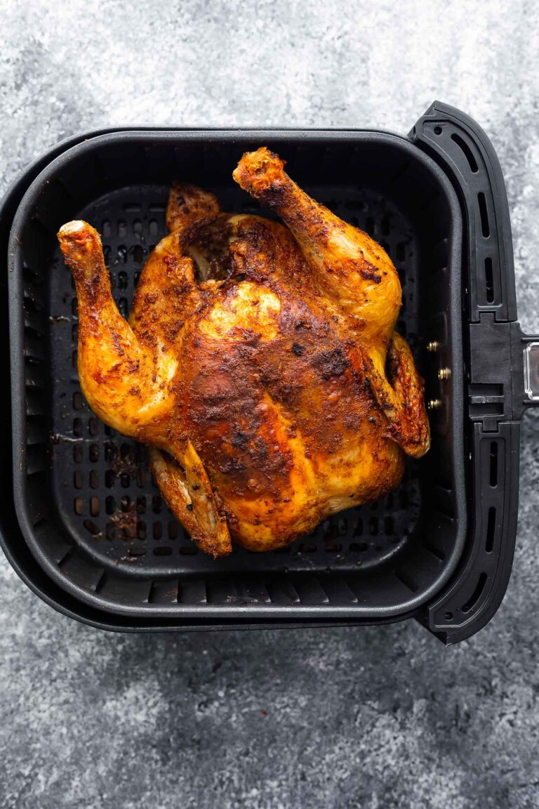 A whole cooked chicken in the basket of an air fryer.