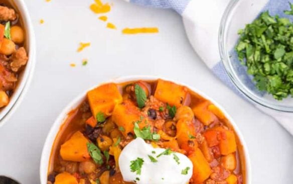 A bowl of butternut squash and turkey chili topped with sour cream.