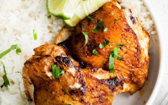 Cilantro and lime air fryer chicken thighs on a plate with rice and lime.