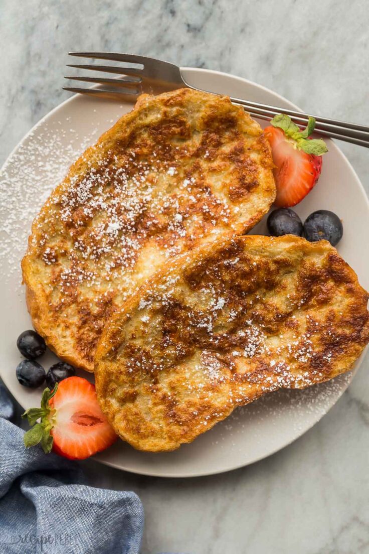 This Easy French Toast Recipe is a classic breakfast recipe that's ready in just minutes! Crusty slices of French bread are doused in a lightly sweetened batter and cooked until soft in the middle and golden-brown and crispy on the outside. #breakfast #recipes | breakfast ideas | breakfast recipes | brunch | french bread | easy recipes | christmas breakfast overhead image of two slices of french toast on grey plate with fresh berries