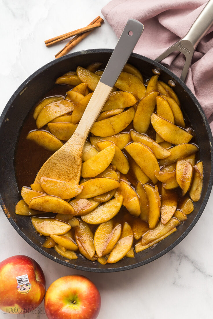 overhead image of fried apples in a black skillet with a wooden spoon