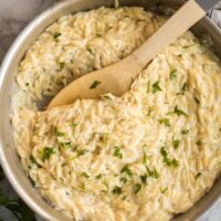 overhead image of skillet of garlic parmesan orzo pasta with wooden spoon stuck in