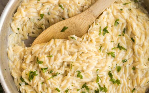 overhead image of skillet of garlic parmesan orzo pasta with wooden spoon stuck in