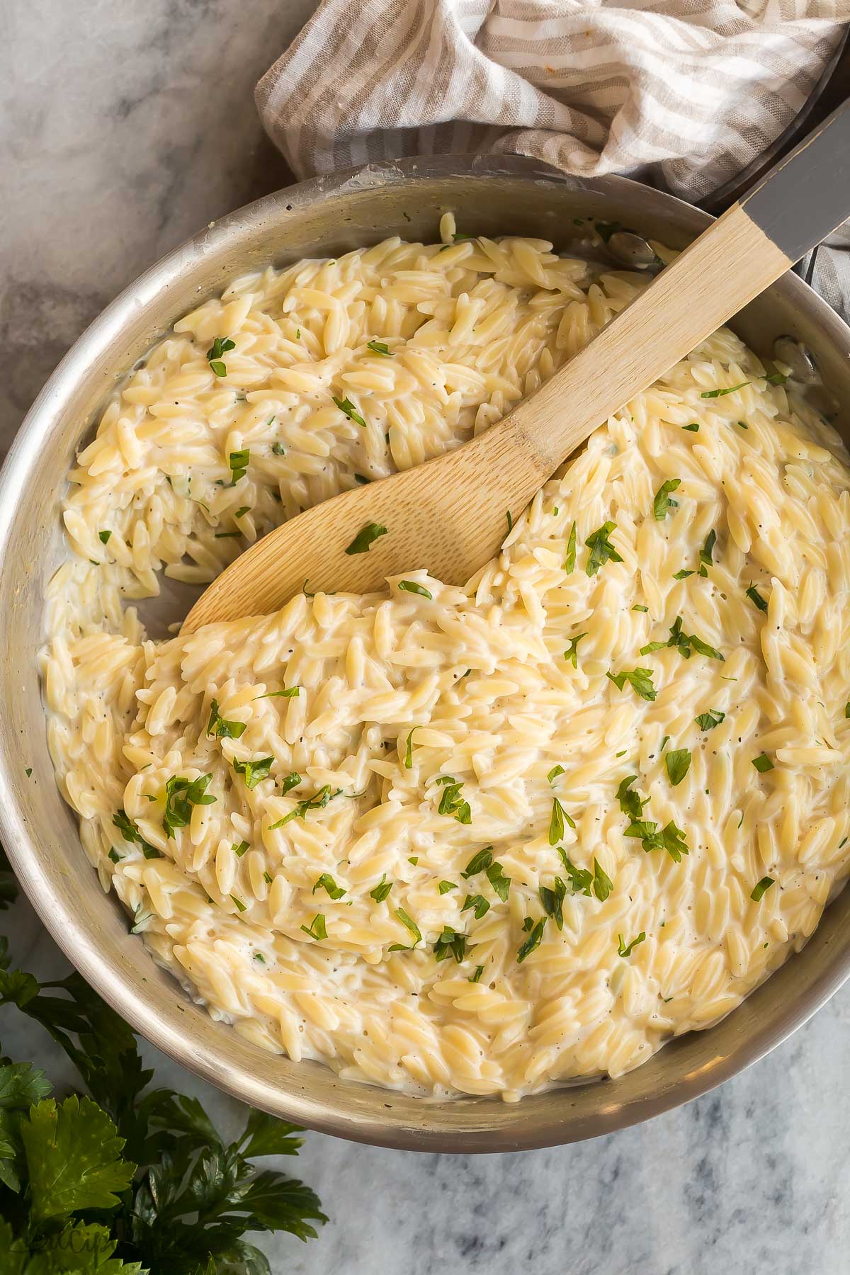 overhead image of skillet of garlic parmesan orzo pasta with wooden spoon stuck in