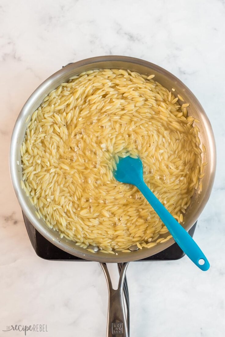 cooked orzo in skillet with blue spatula
