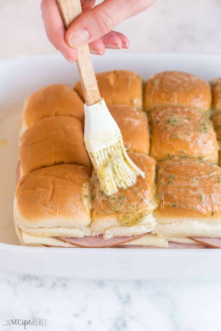 brushing melted butter on top of ham and cheese sliders