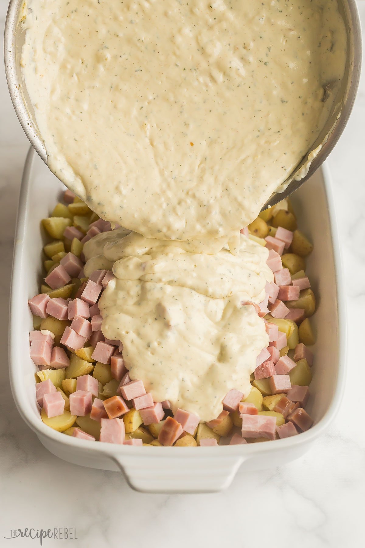 creamy sauce poured over ham and potatoes in casserole dish
