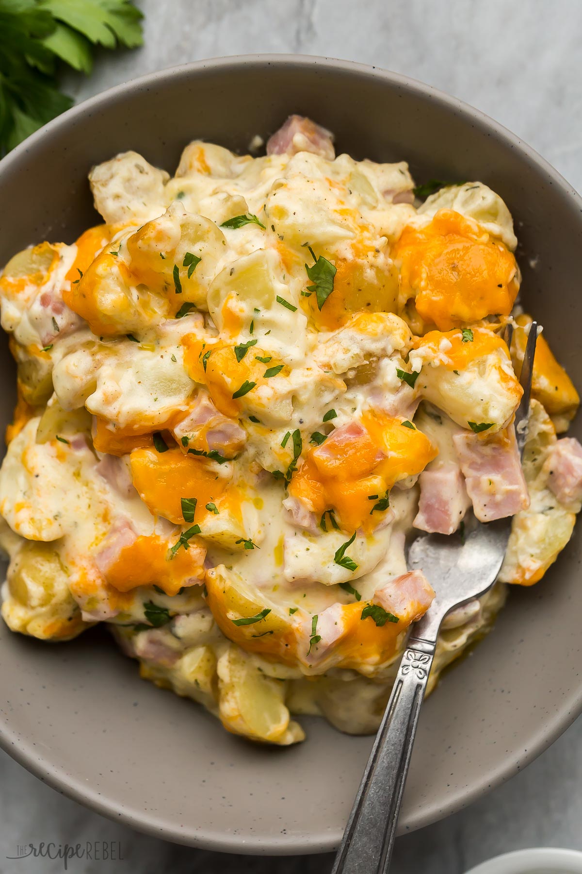 close up overhead image of ham and potato casserole in grey bowl with fork