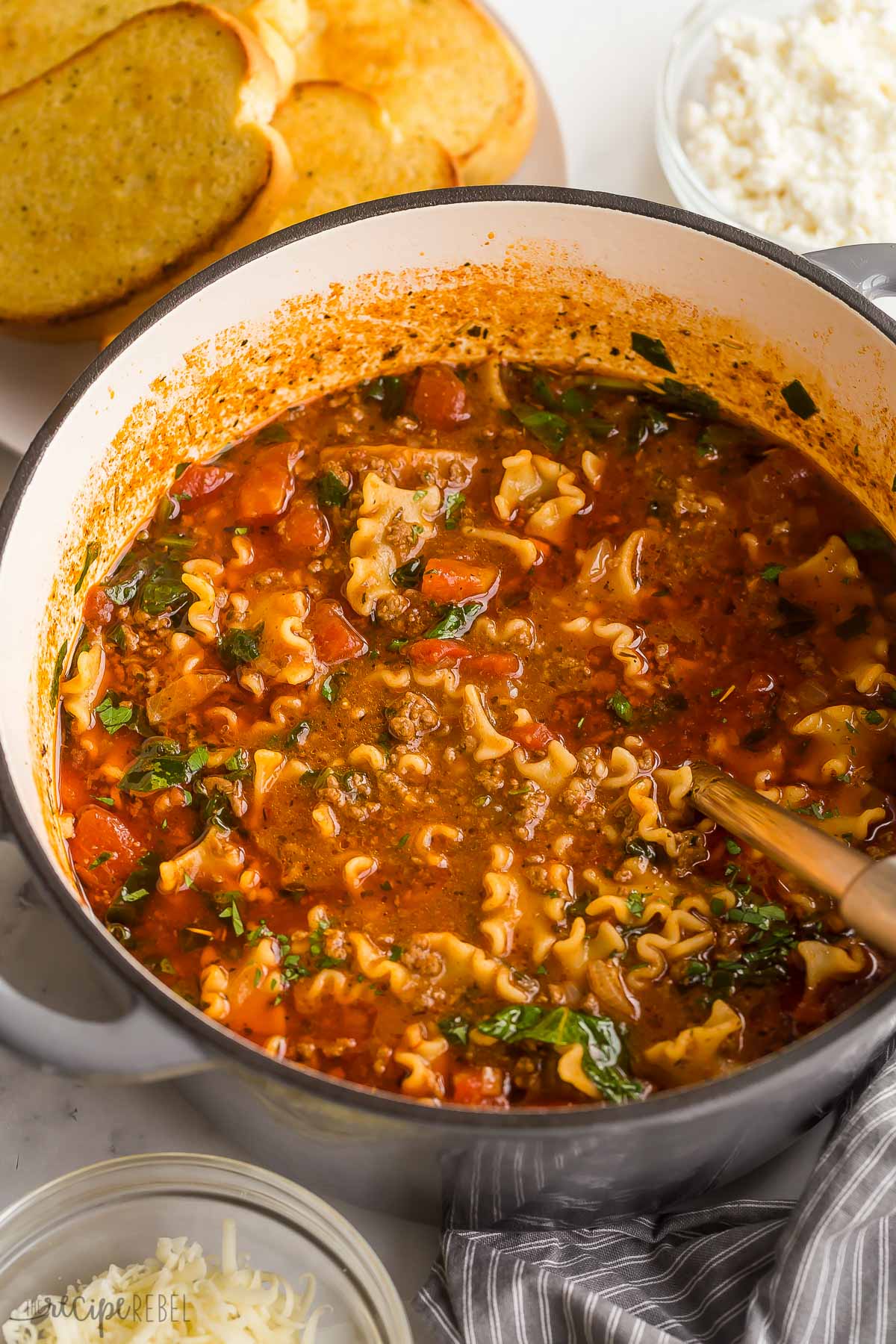 close up image of lasagna soup in dutch oven with garlic bread in the background