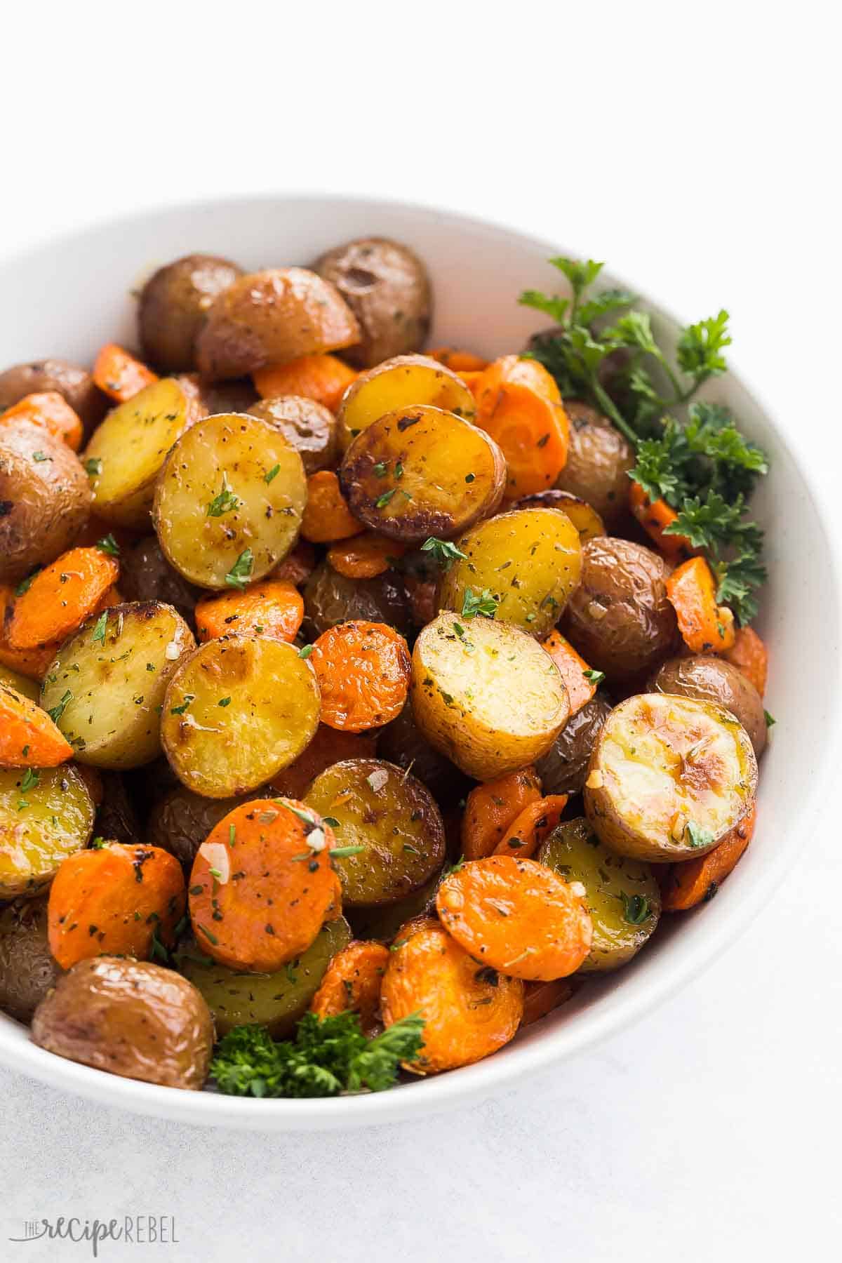 close up image of roasted carrots and potatoes in a white bowl sprinkled with parsley.